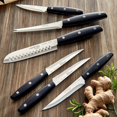 Set of knives with black handles on a wooden surface, including a piece of ginger.